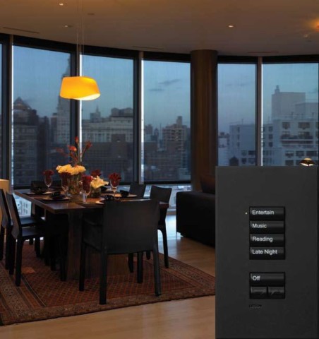 Lutron shades almost fully lowered in a living room overlooking the city with an inlaid photo of a Lutron keypad. 