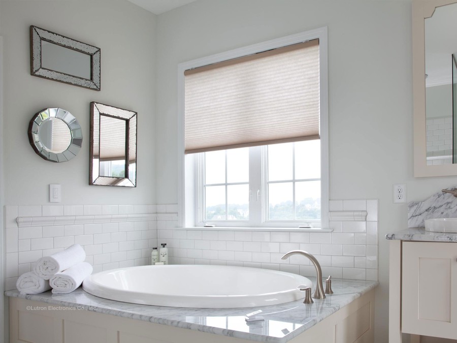 bathtub in front of a window with motorized blinds halfway drawn.