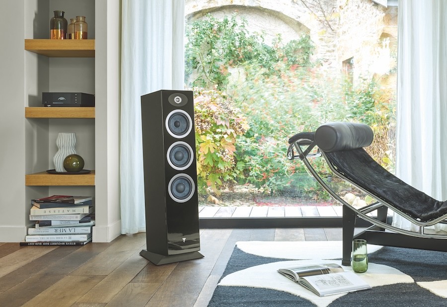 A Focal floor-standing speaker in front of a large window showcasing a lot of foliage.